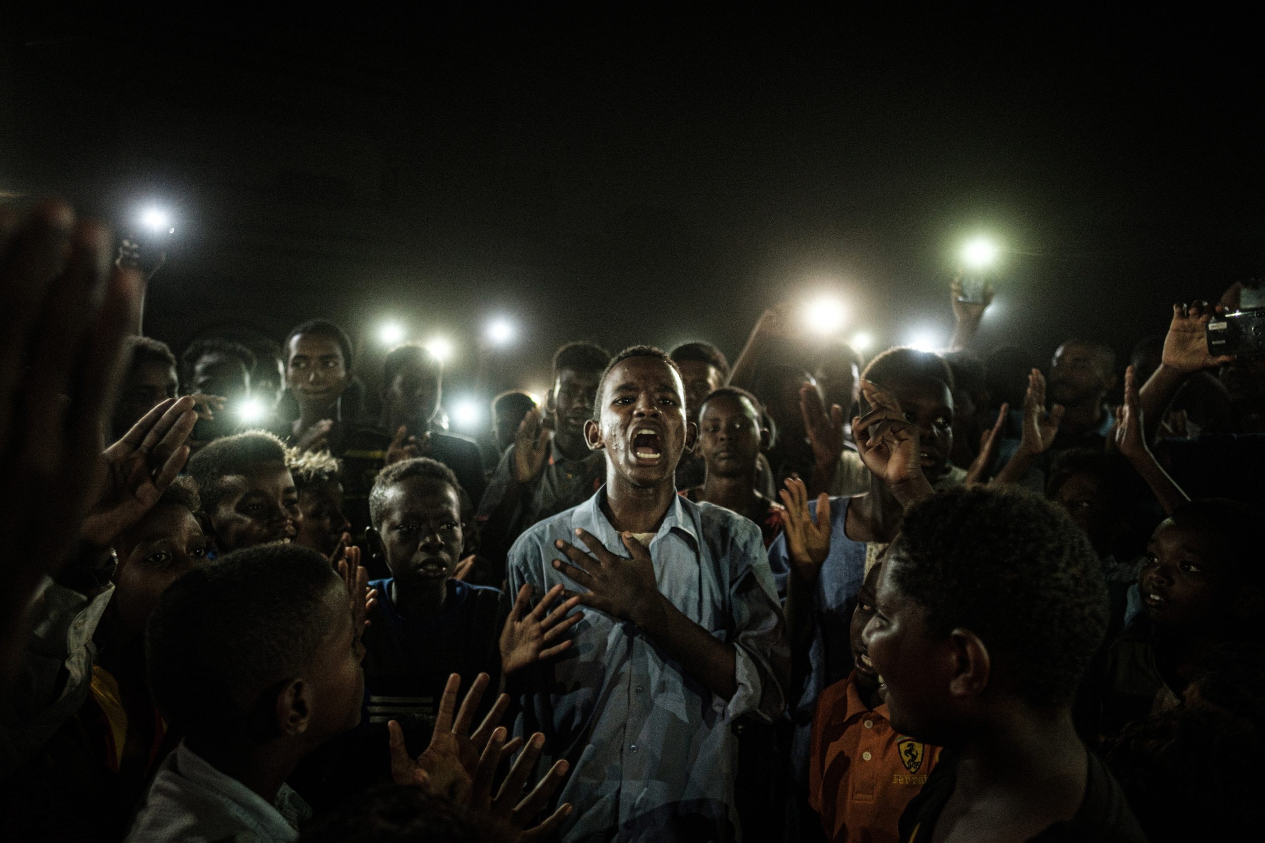 Um rapaz, iluminado por telemóveis, a recitar poesia. Imagem de protesto no Sudão vence prémio World Press Photo