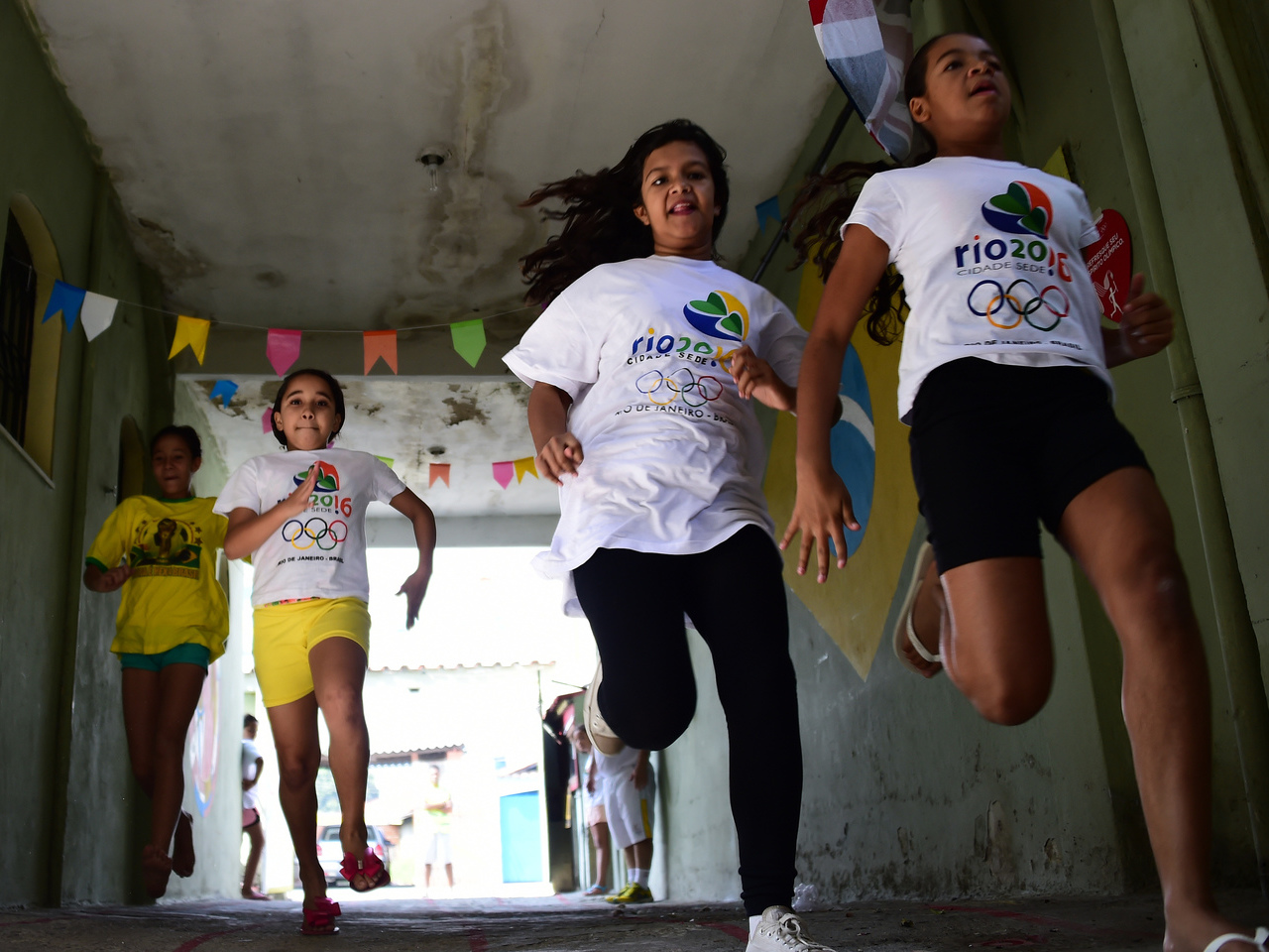 Sports enthusiast Jarbas Meneghini (R) poses with children from his neighborhood in front of his house in Campo Grande, Rio de Janeiro, Brazil on August 9, 2016. Menenghini, a 47-year-old mechanic who when he was young wanted to be a footballer, has turned his home into a sort of museum of the Olympic Games and the football World Cup and where every Sunday since last month, the children from the neighborhood gather to play the "Olympic Games". / AFP PHOTO / TASSO MARCELO
